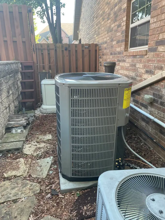 A newly installed American Standard condenser on its pad beside a brick home